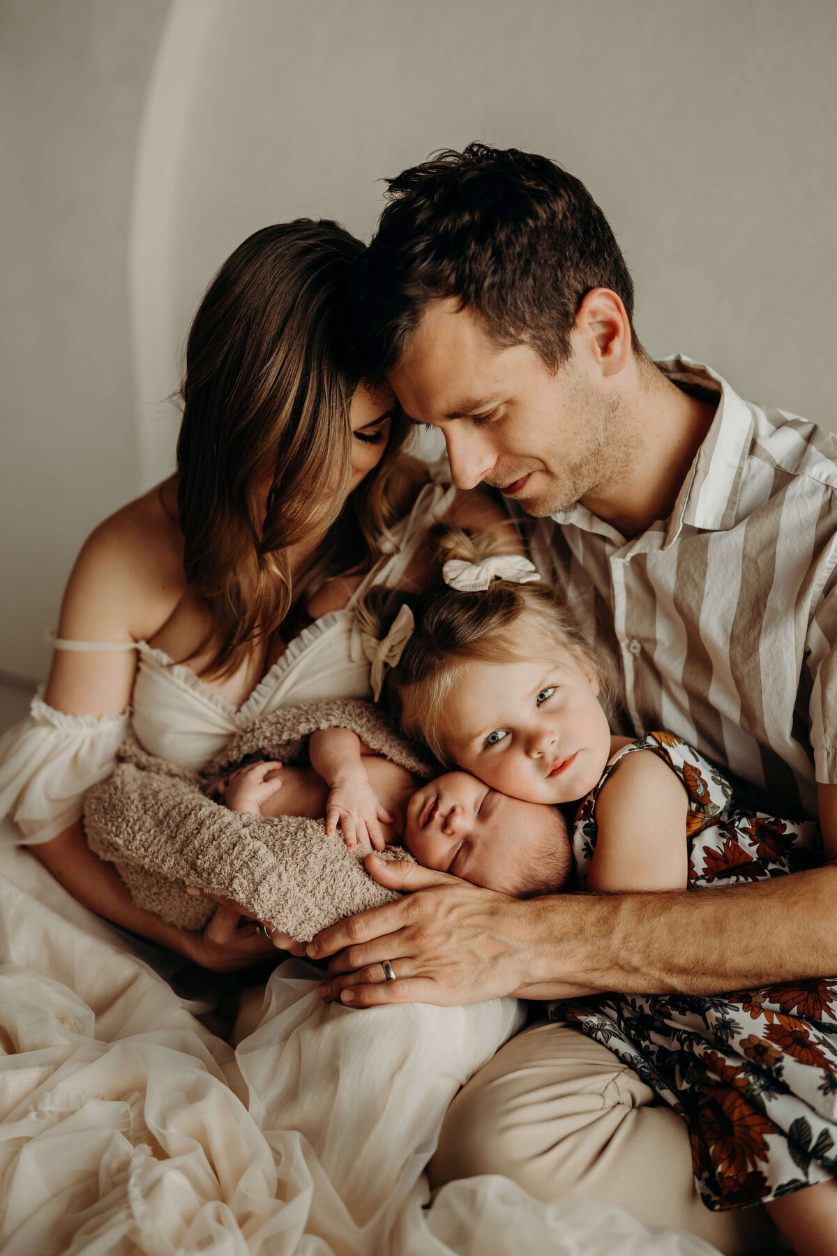 emotive family looks at baby brother being hugged by his toddler sister during a studio photography session