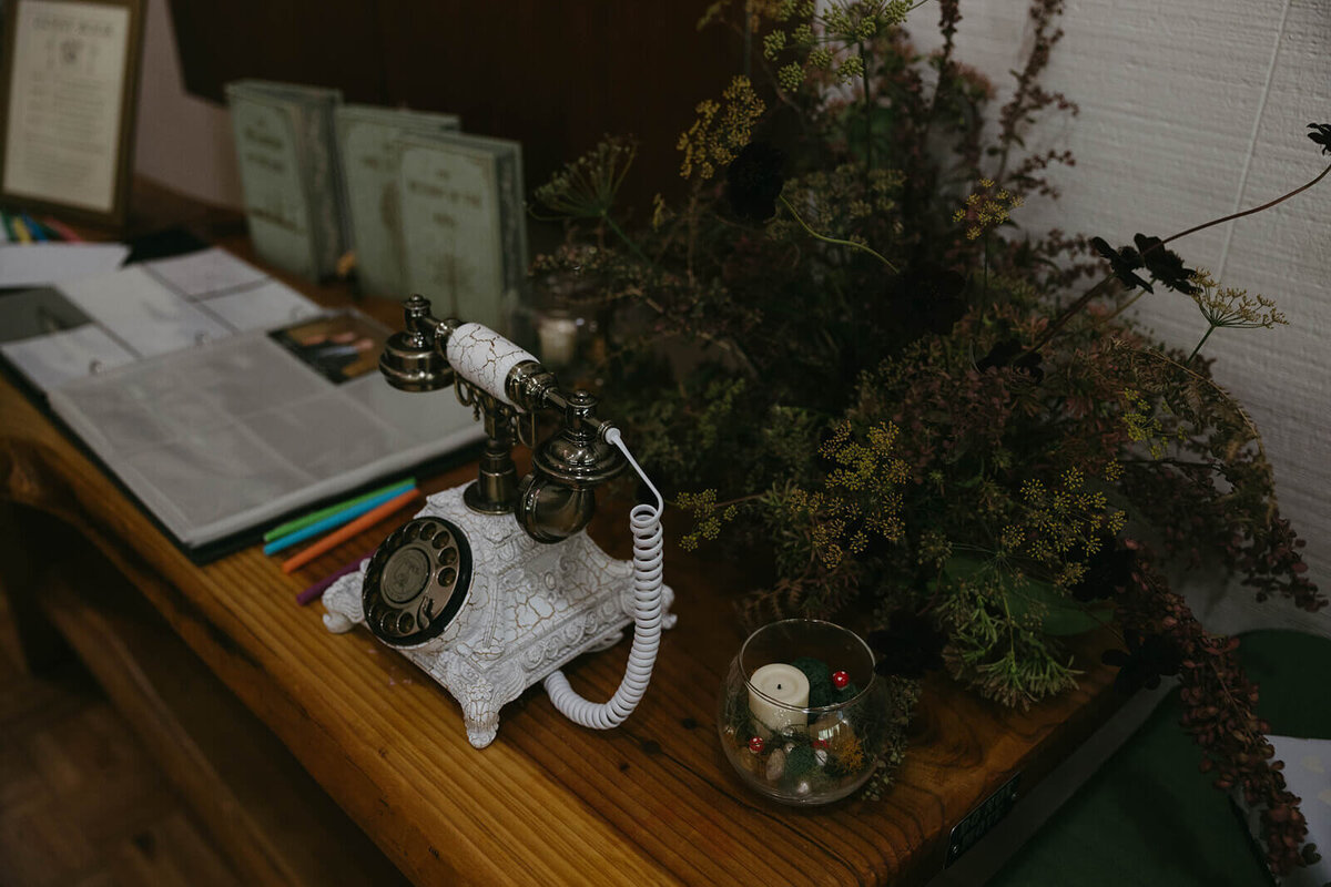 Wedding details including a white vintage phone used for an audio guestbook, candles and greenery.