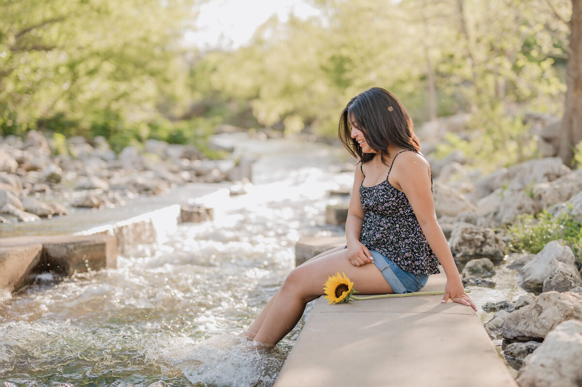Girl sits on the edge of the water at Confluence Park in San Antonio during senior pictures.