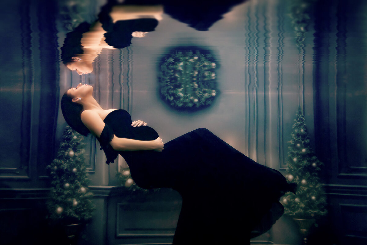 Elegant underwater maternity photo featuring a woman in a black gown floating effortlessly, her reflection softly merging with festive decor. This Dallas underwater maternity photographer captures a serene moment surrounded by a dreamy, luxurious setting.