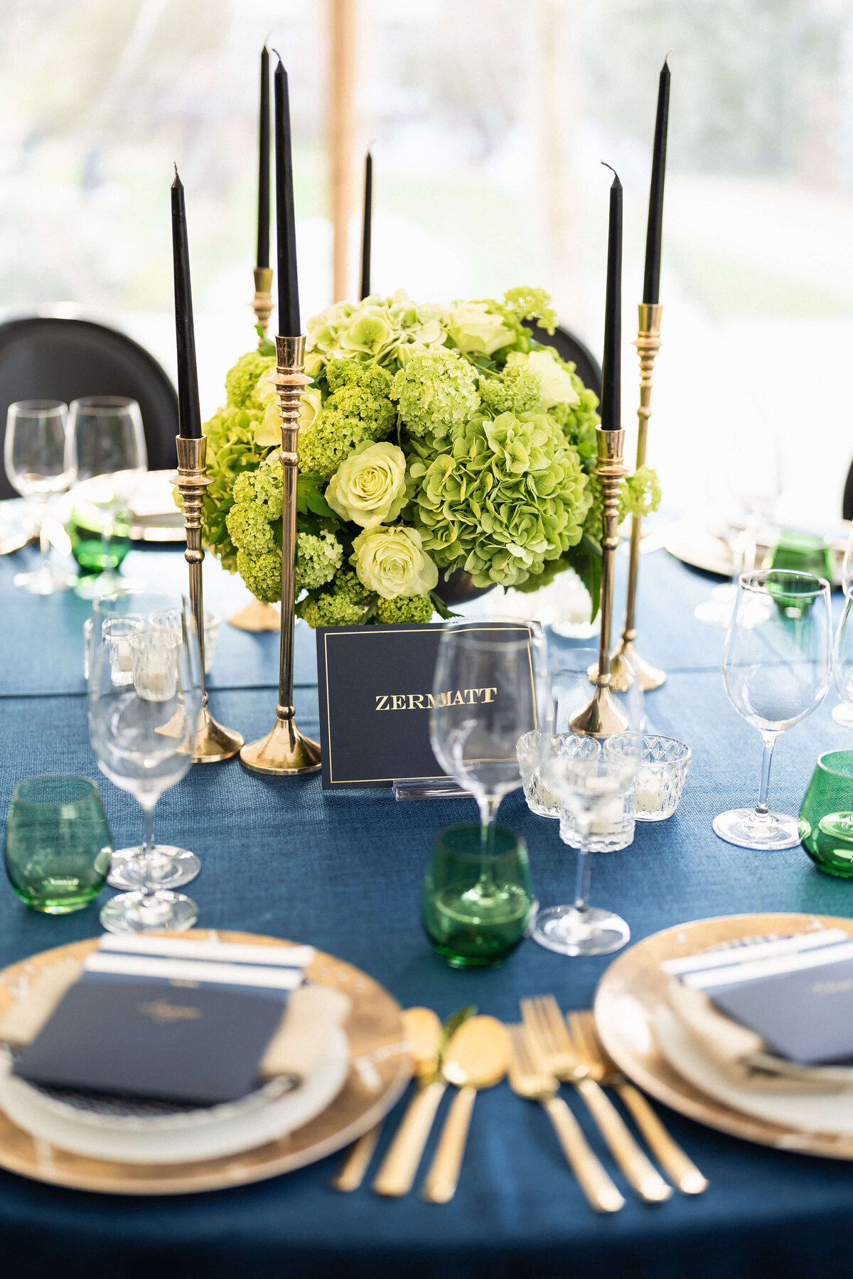 lime green flower arrangements in the centre of a round dinner table laid with navy blue linen and gold table settings for a birthday party at avington park