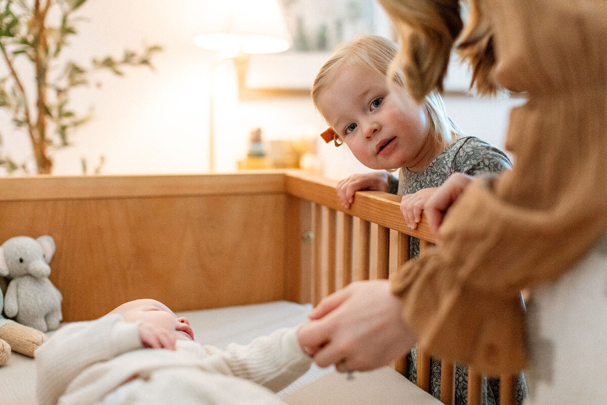 Mother and child admiring newborn baby in crib with beautiful lighting - Sara James San Antonio newborn photographer documents precious family introduction moments and early bonding during gentle home sessions