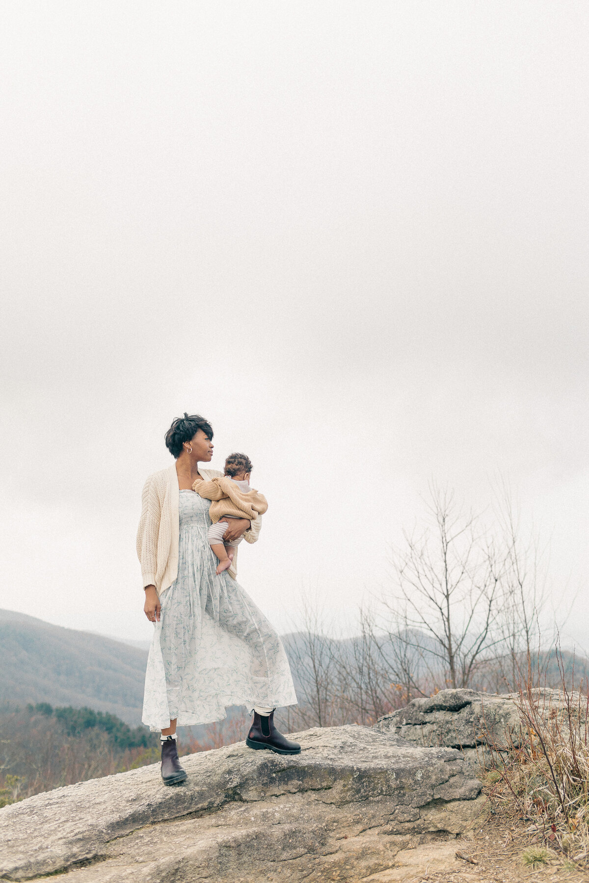 A portrait of a mother in a strong stance as she sways her baby at a Kansas City scenic overlook during a peaceful outdoor newborn photography session.