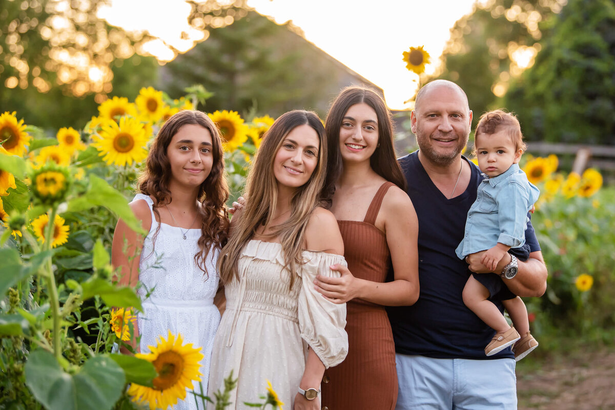 up-close photo of mom and dad with their two daughters and baby boy in a sunflower field in the golden hour for their family photos in Burlington