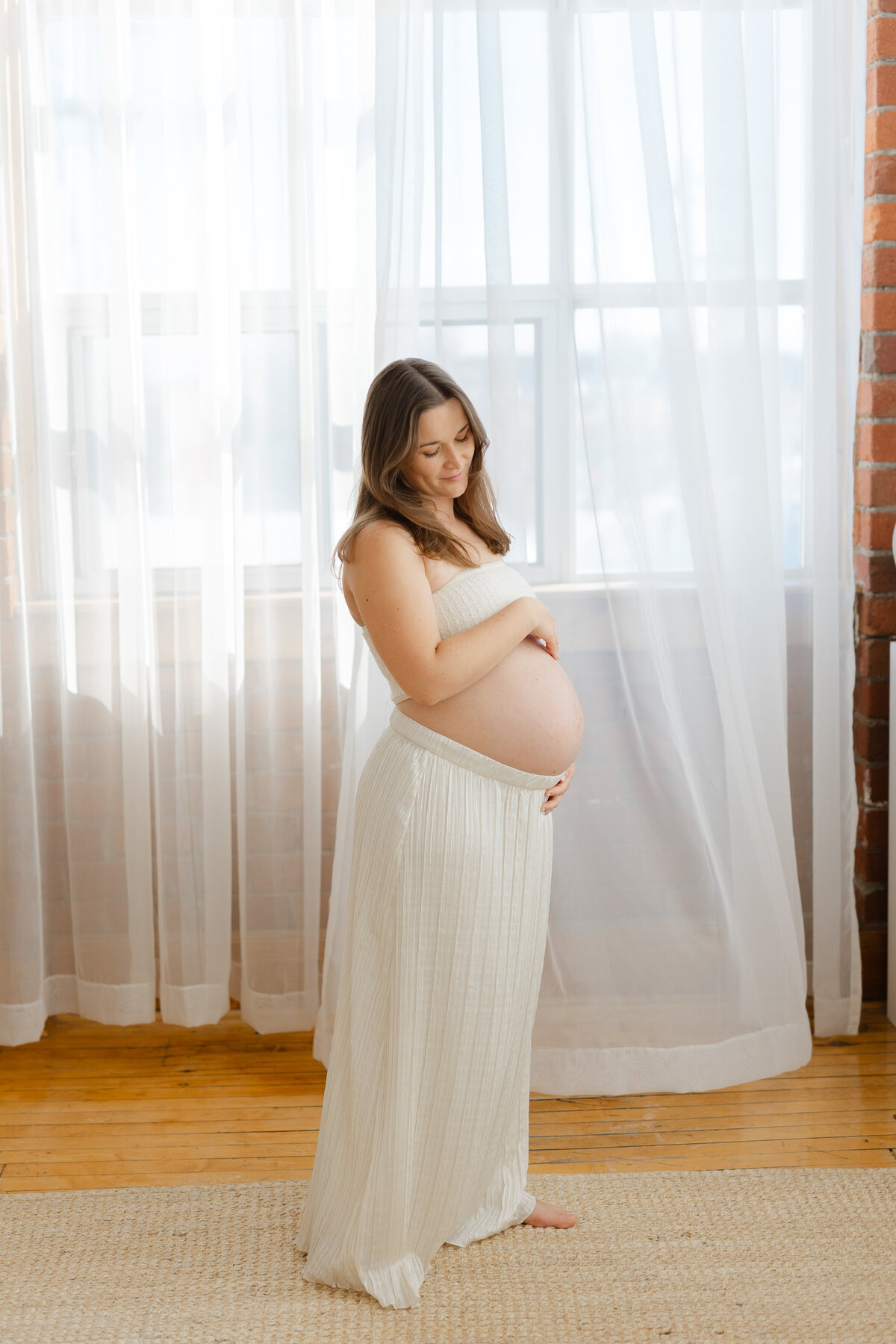 A pregnant mom is looking down on her belly with her hands on her pregnant bump in a Toronto maternity session