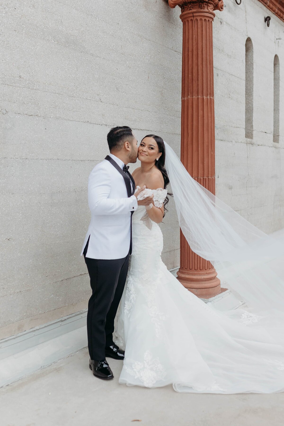 Bride in off-shoulder lace gown smiles as her groom kisses her at Lightner Museum, St. Augustine Florida | Best Wedding Photographer St Augustine