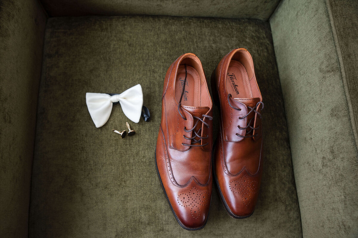 A classic pair of brown leather shoes and a crisp white bowtie, carefully placed for the big day.