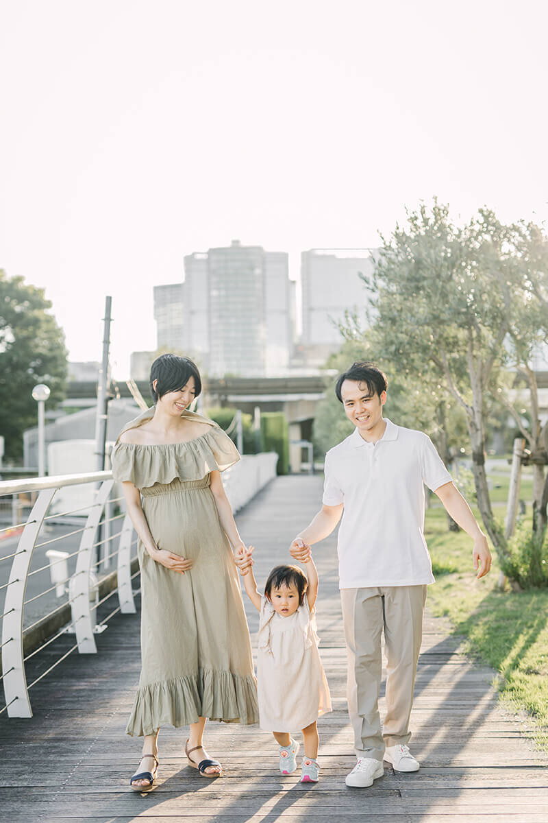 A family maternity session in Tokyo Japan by Yukika Ishikawa Photography. Mother and father holding hands of their baby girl while the mother is putting her hands on her bellyl.