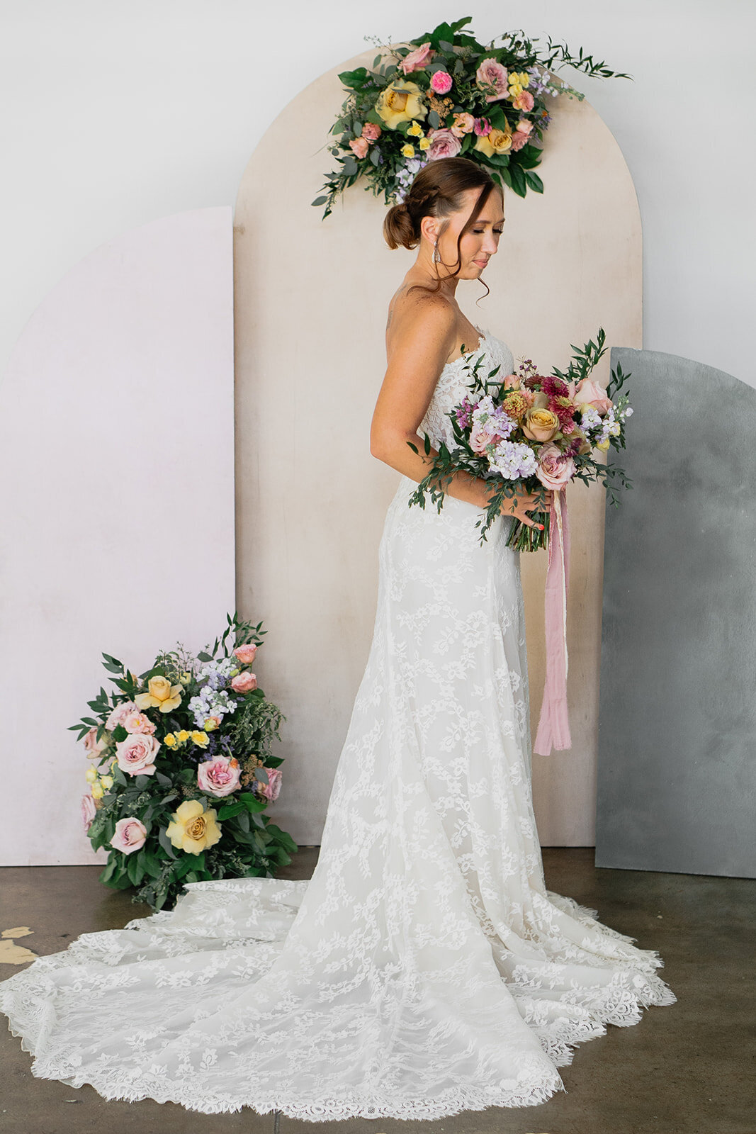 bride standing in front of arch with bouquet and florals