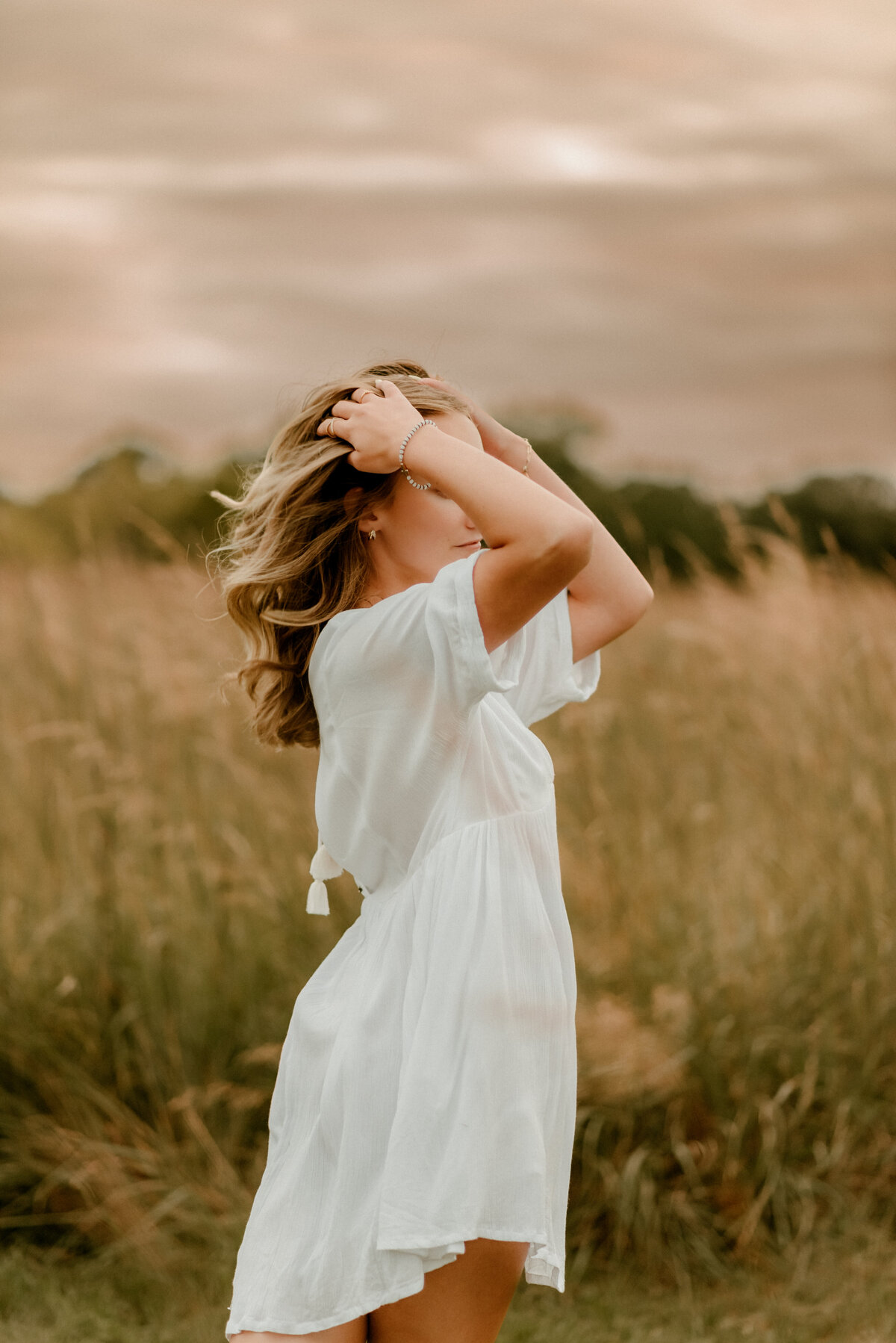 Teen girl laughing and twirling in a field during golden hour senior session near Forest Lake, MN.