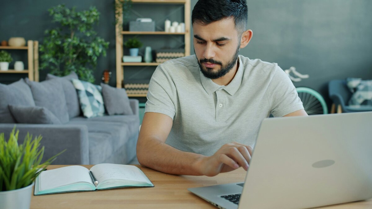 Person reviewing a notebook beside a laptop at a desk