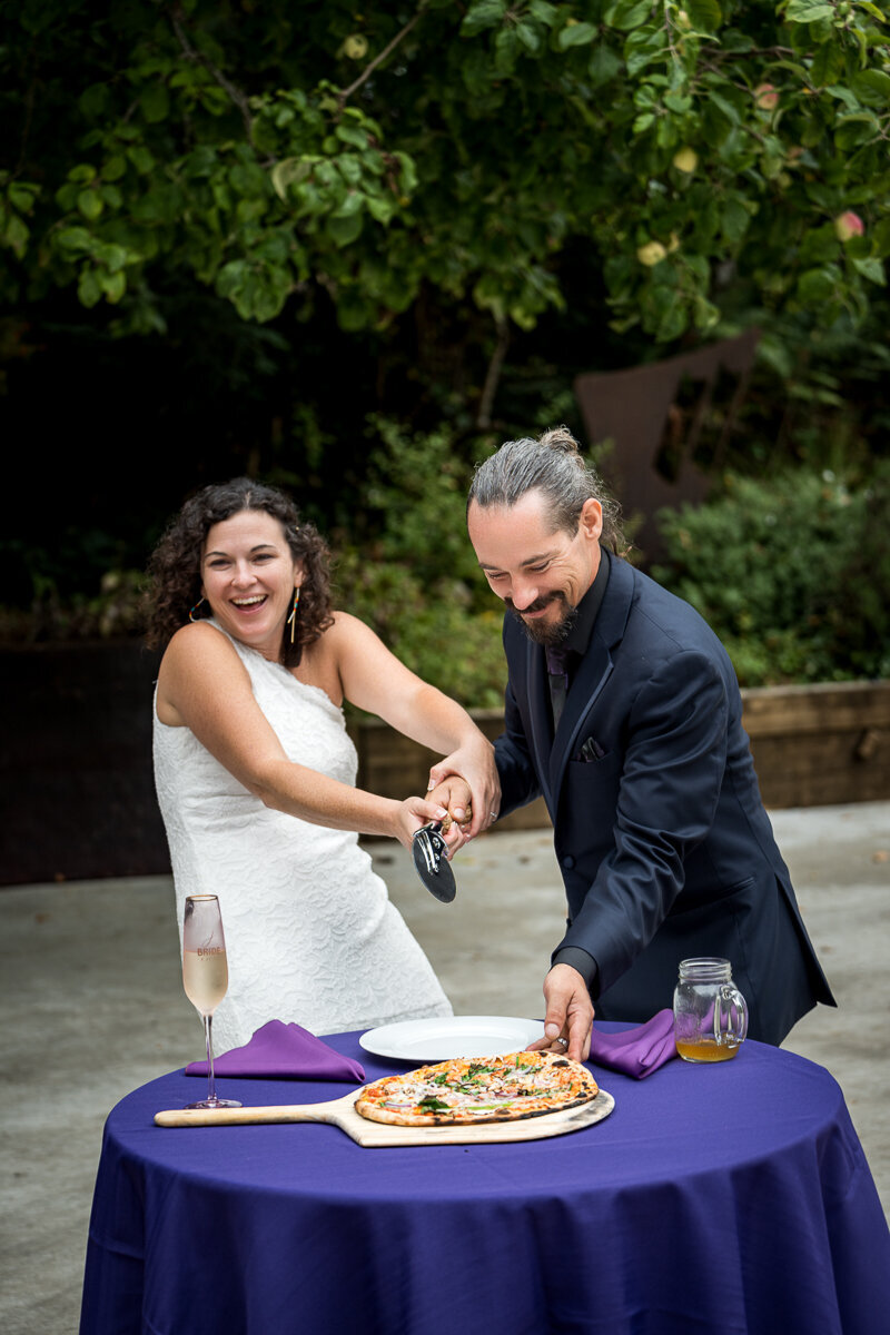 A playful and memorable wedding moment as the bride and groom cut into a delicious pizza instead of a traditional cake in Arcata, CA, showcasing their fun-loving personalities.