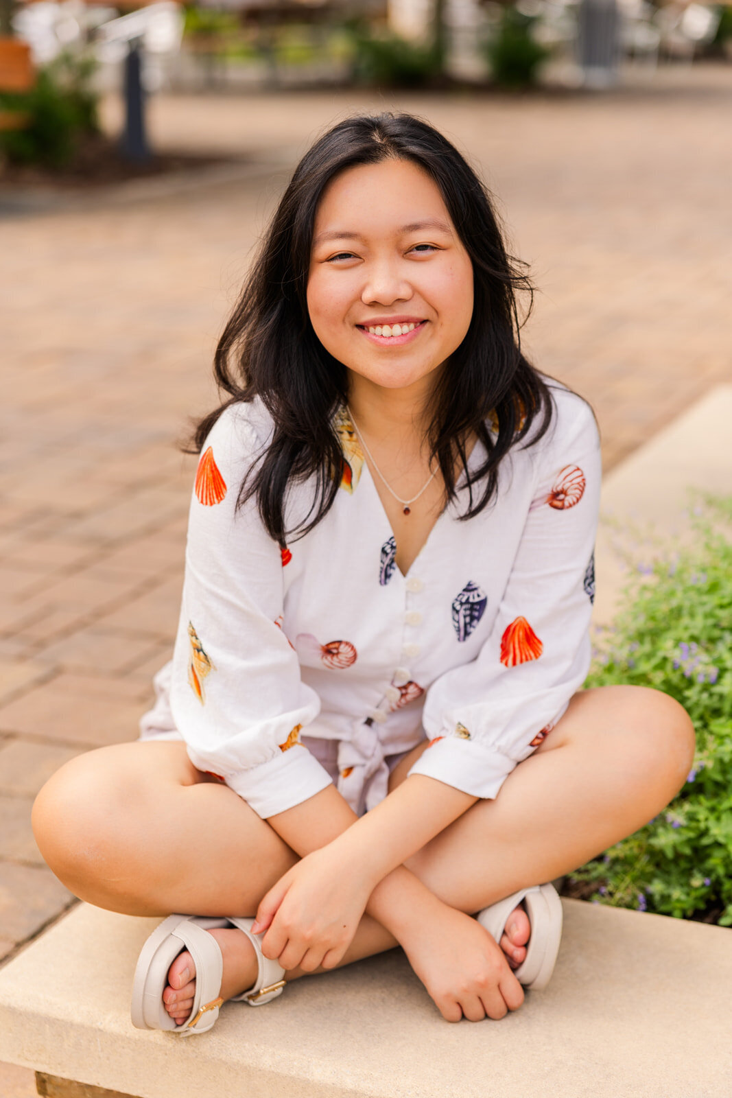 teenager sitting criss cross on a street wall hands resting on front of her during senior portraits