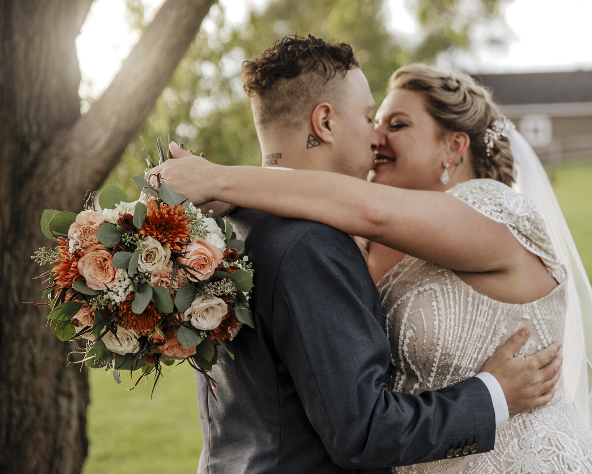 A joyous couple on their wedding day sharing an embrace outdoors, with the bride holding a beautiful bouquet of flowers taken by jen Jarmuzek photography a Minneapolis wedding photographer