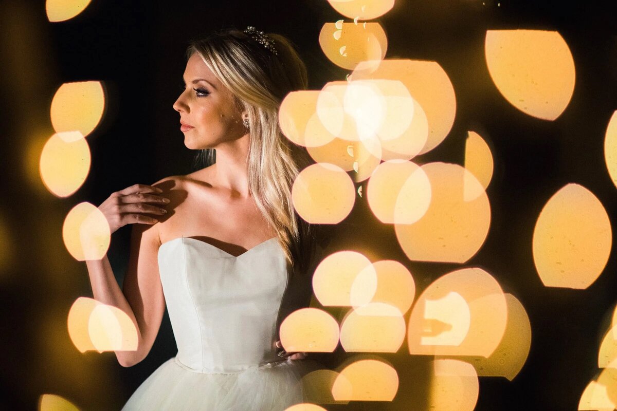 A bride stands illuminated by a myriad of soft lights, her silhouette casting a glow against the dreamy background.