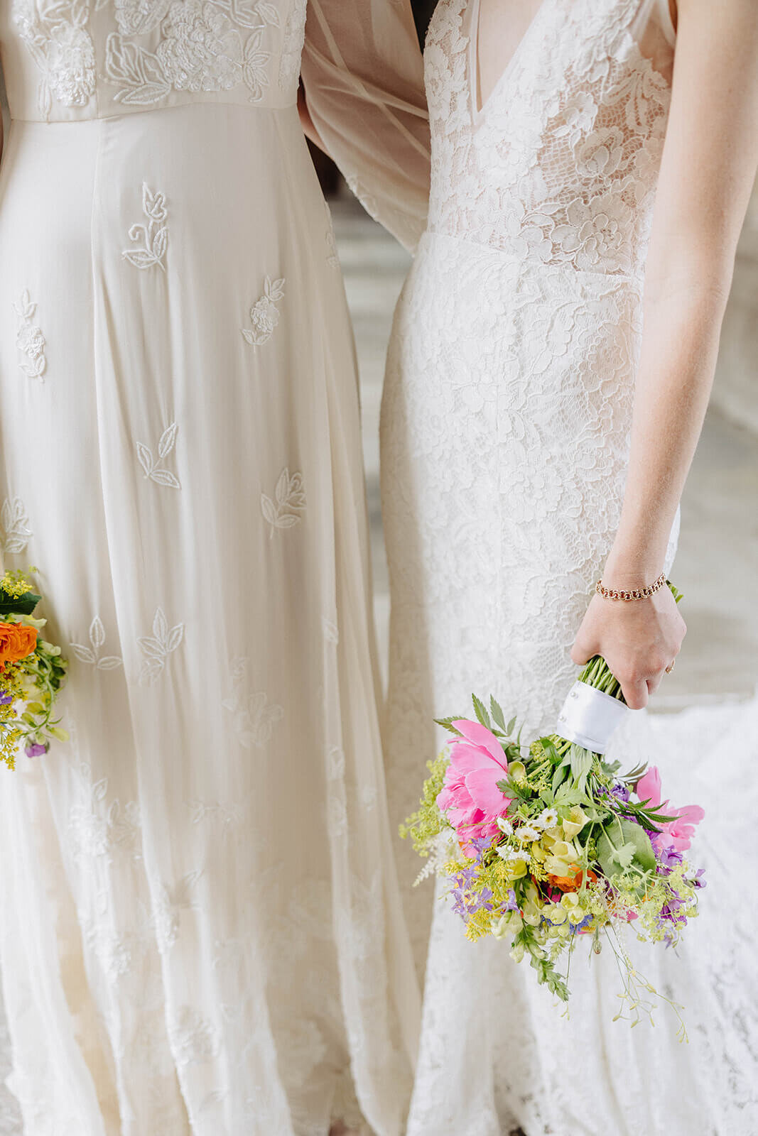 Two brides in white wedding gowns holding colorful bouquets