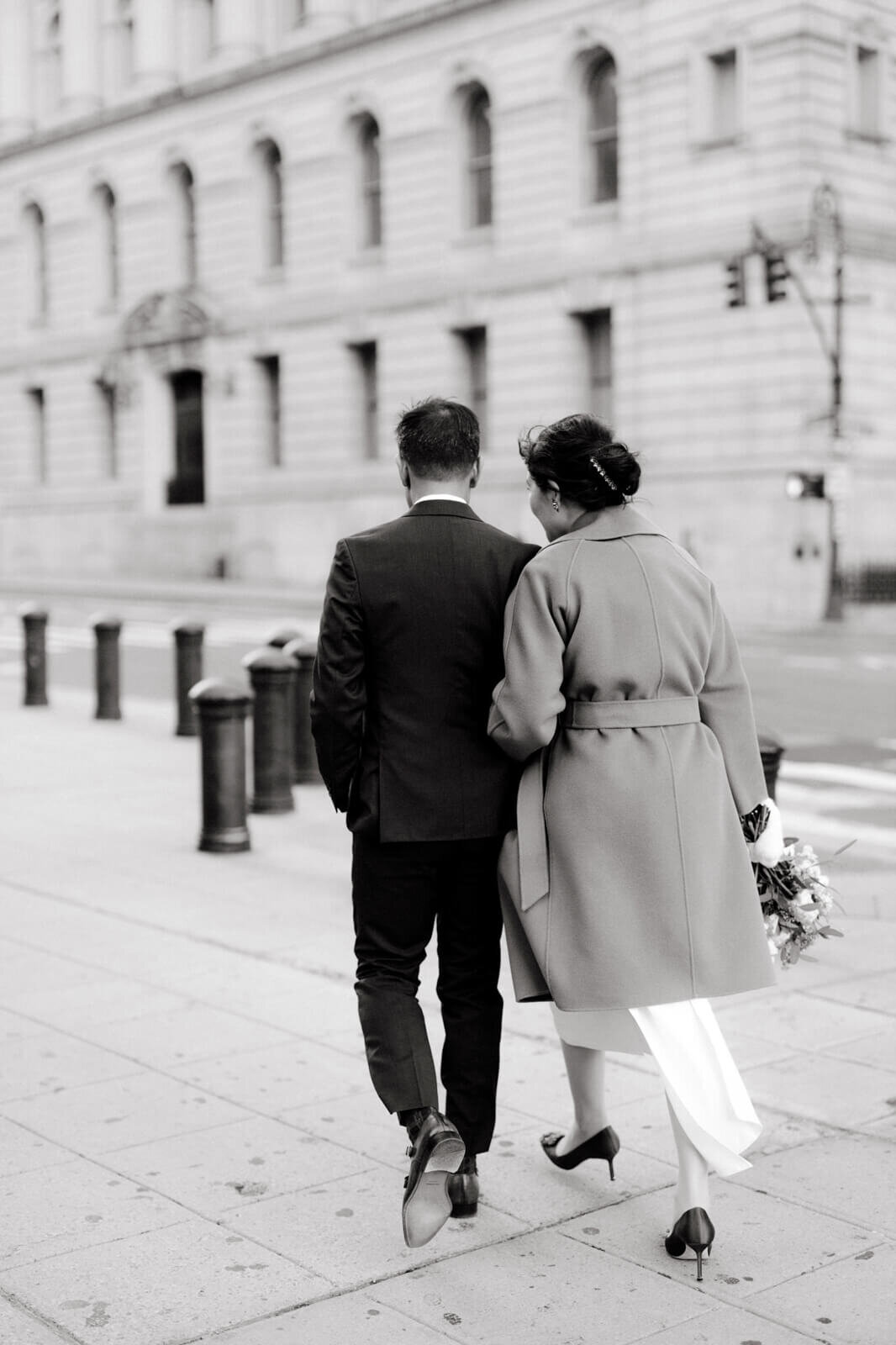 Black and white, back view photo of the bride and groom walking in the streets of New York.