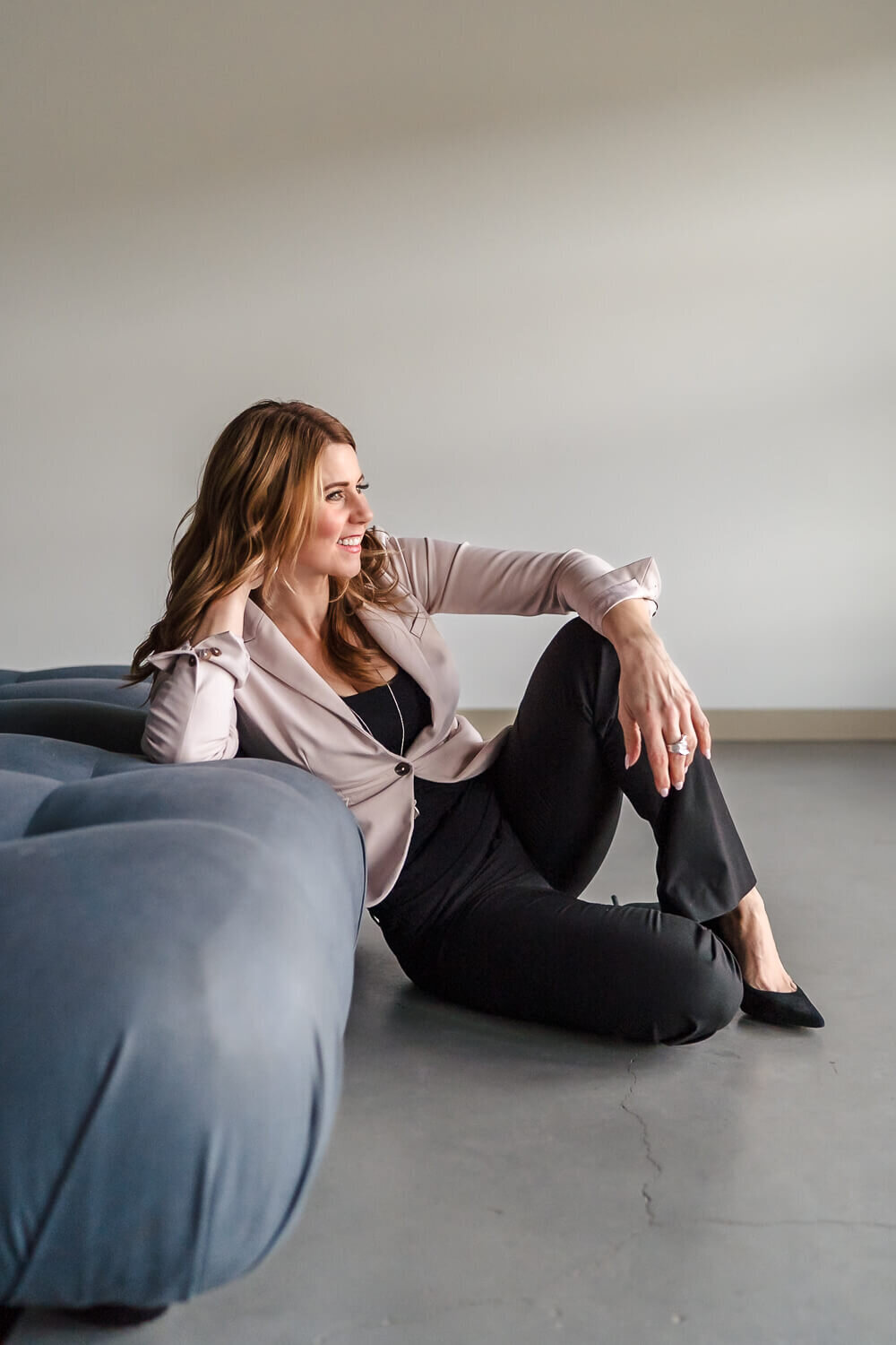 Woman in grey sweater and jeans reclining in chair during indoor headshot session