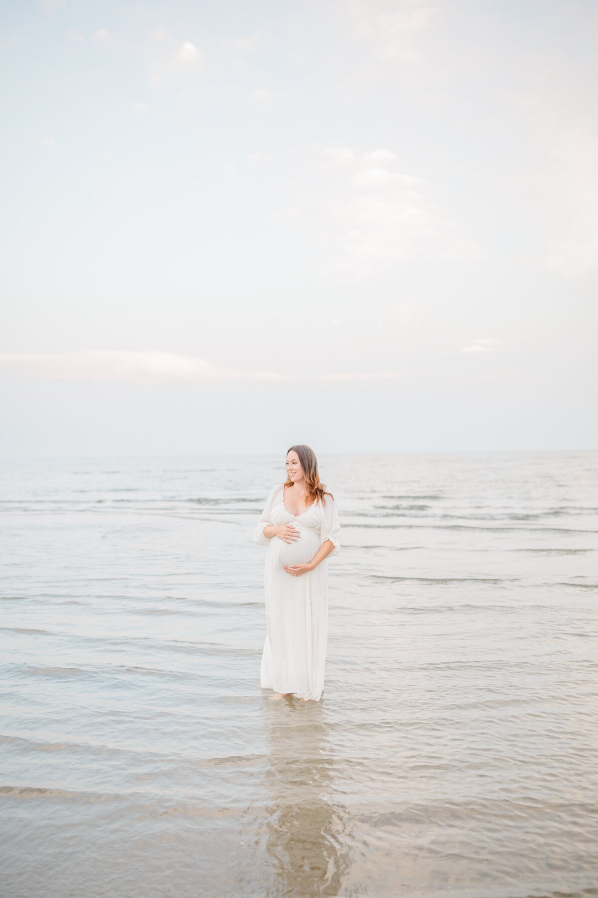 Wrapped in flowing lace, a mother stands barefoot on a rocky shoreline, the ocean mirroring the vast love in her heart