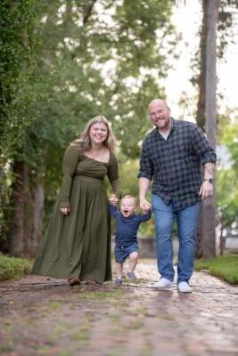Professional family portrait by St Augustine family photographers showing parents and toddler walking on historic brick pathway surrounded by oak trees