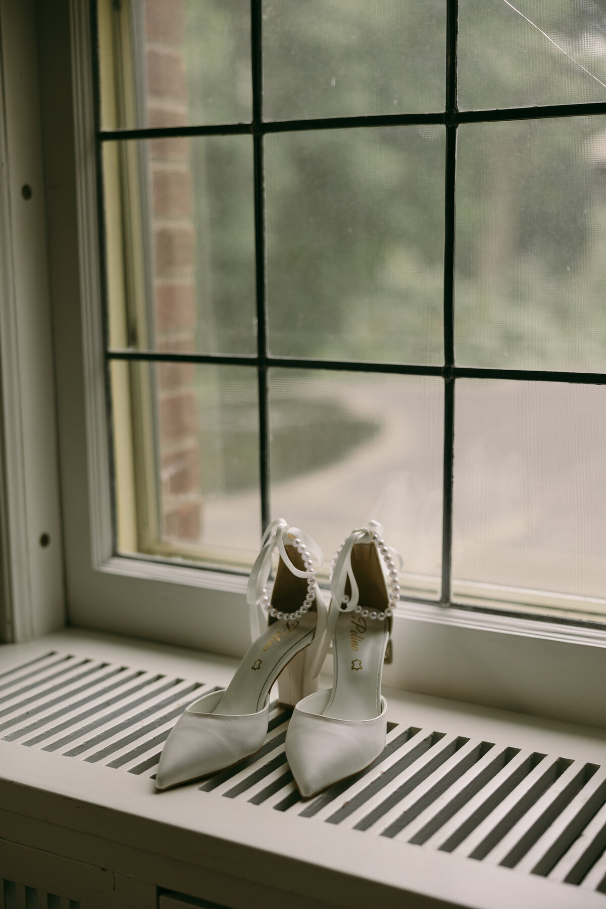 a paid of white heels sitting atop a radiator cover with a window backdrop