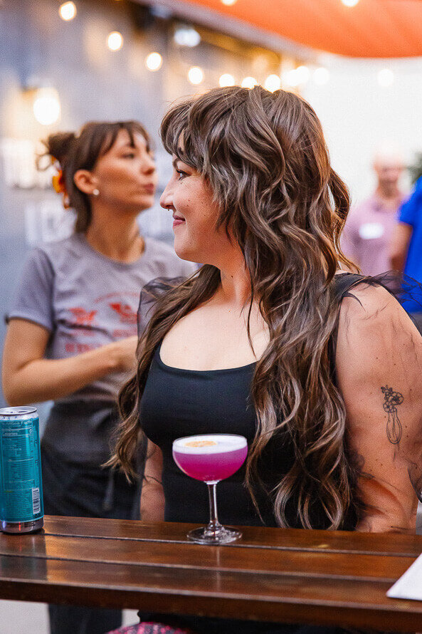 Girl hold pink drink and smiles off to the side.