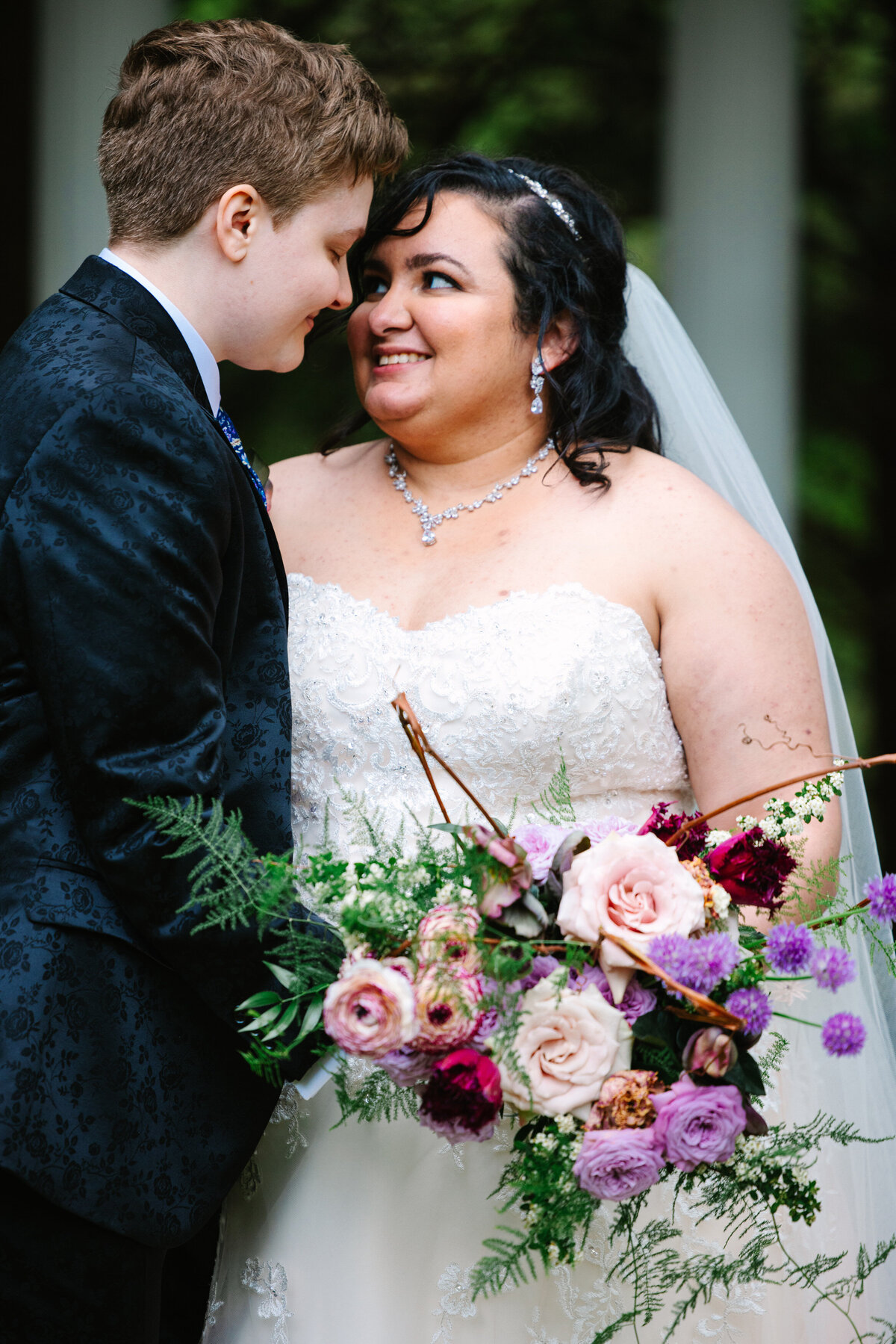 Two brides smiling at each other with wedding bouquet in hand