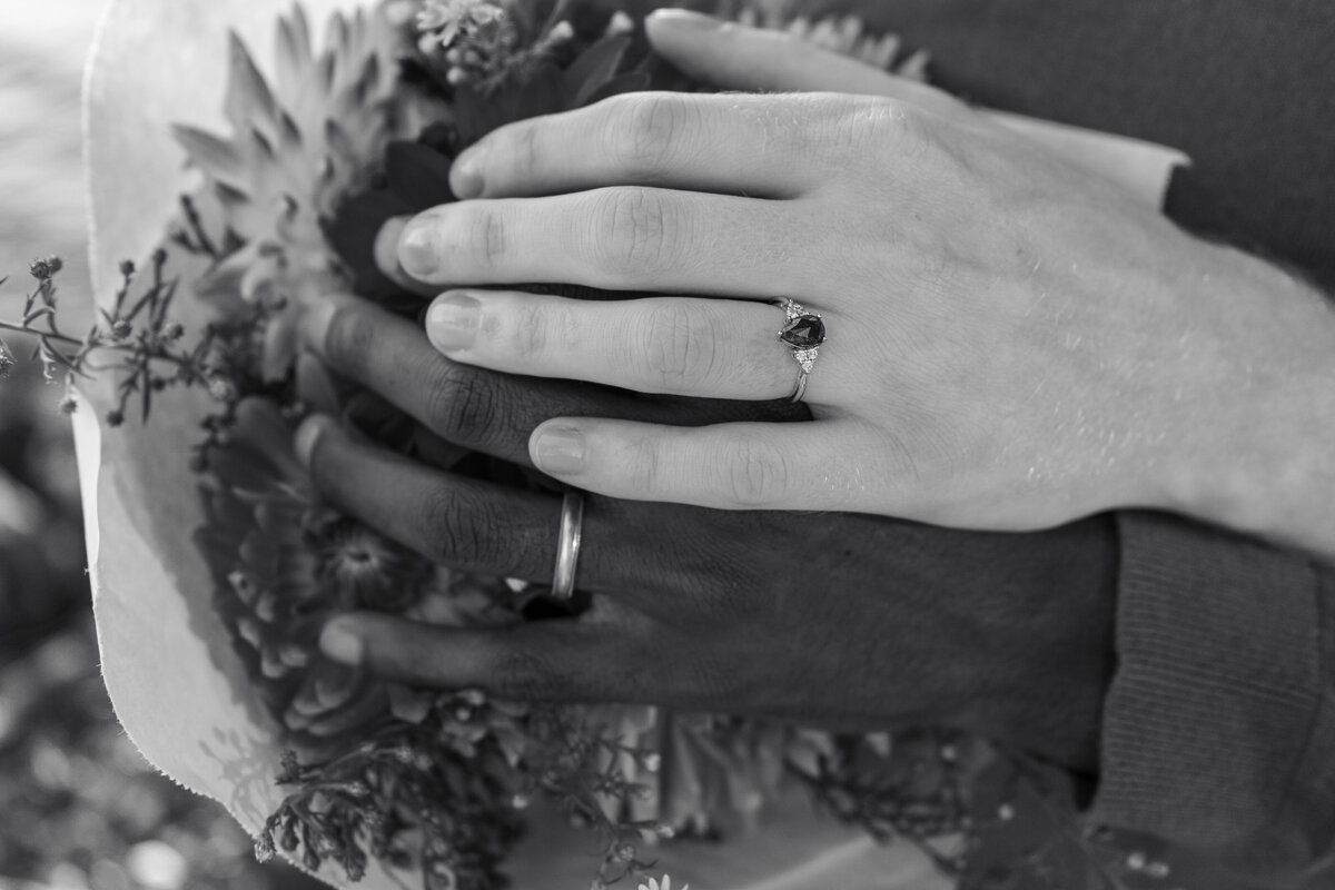 Detail black and white shot of queer engagement rings and flowers in Seattle during sunset