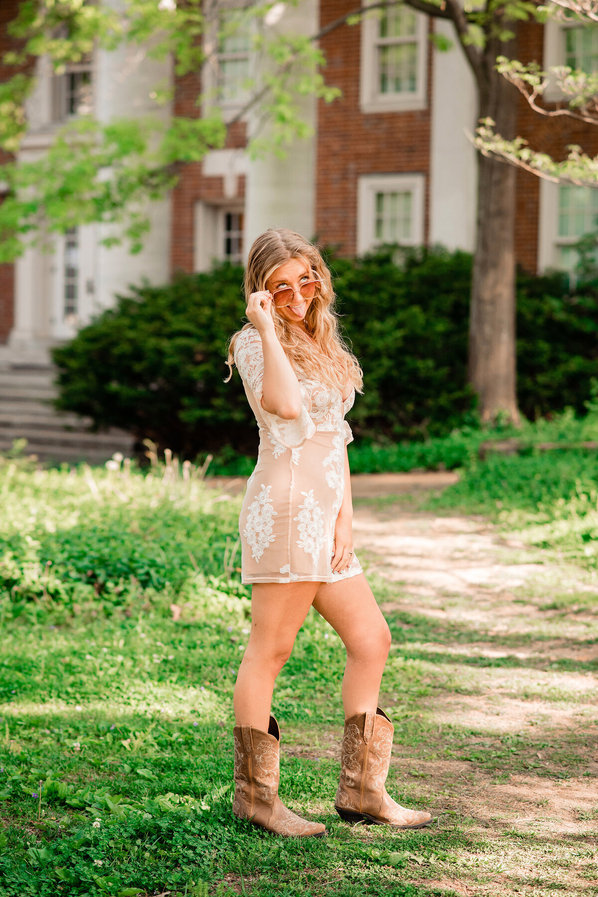 Vanderbilt Senior wearing lace dress and cowboy boots with sunglasses making funny face at camera