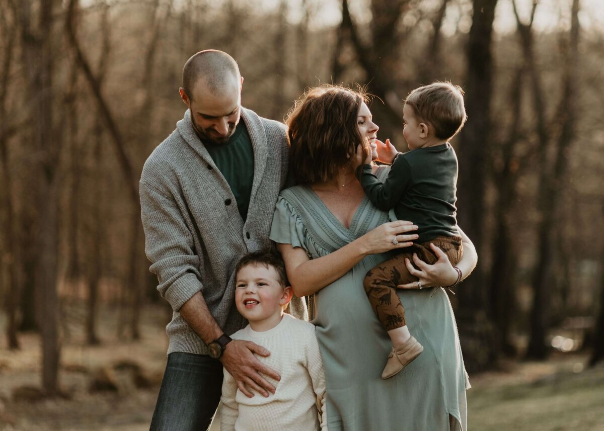 A family poses for a photo in a wooded area, captured by a Pittsburgh maternity photographer.
