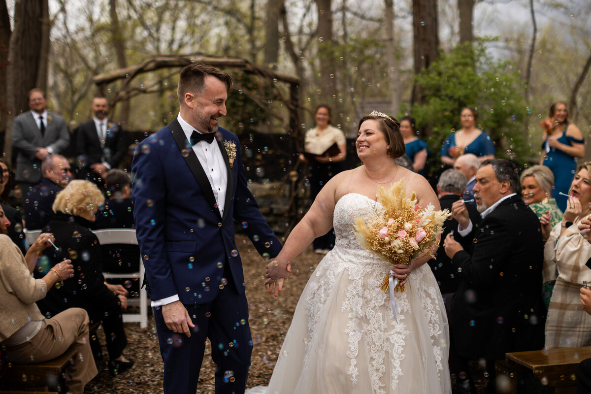 Bride and groom grinning at each other at the end of the aisle, just after saying I do.