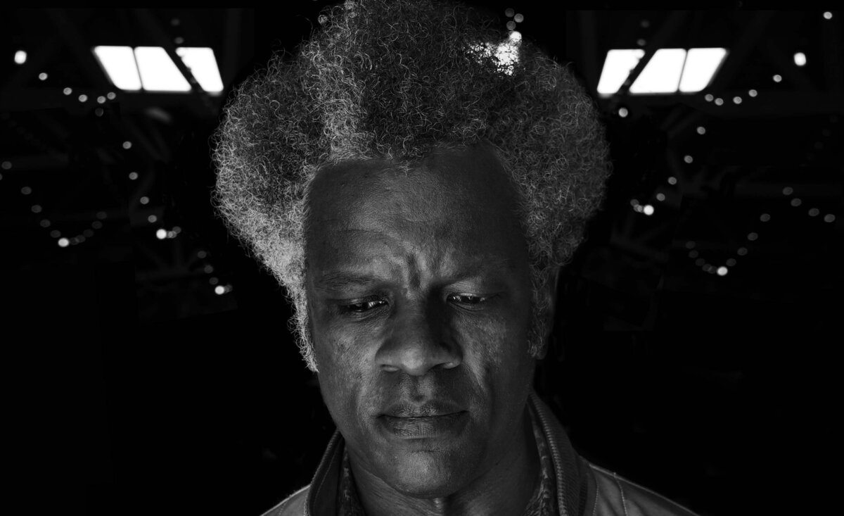 Male portrait close up black and white looking down with grey frizzy hair windows behind head