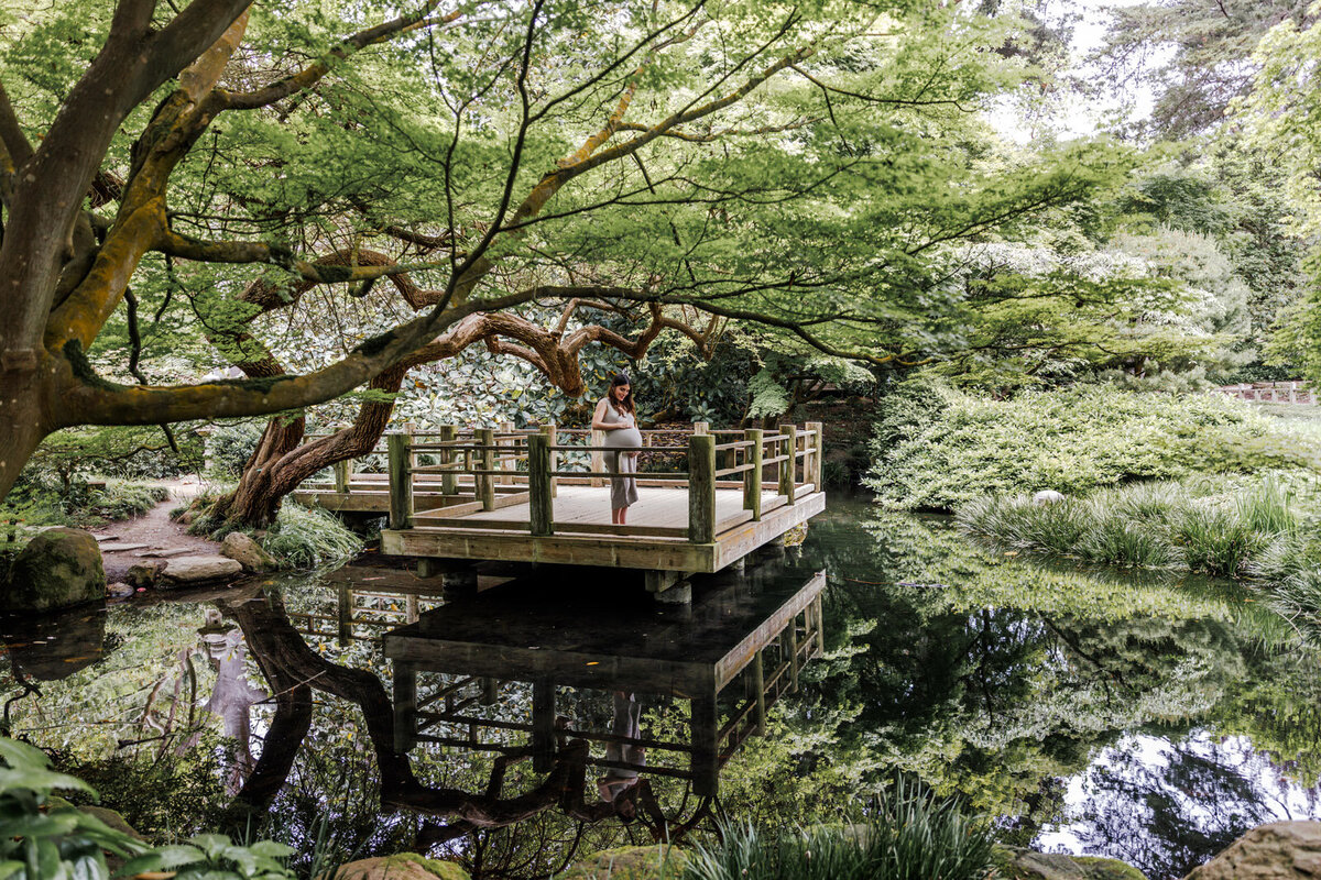 pregnant woman standing on a platform among trees looking down at her baby bump in San Francisco Botanical Gardens