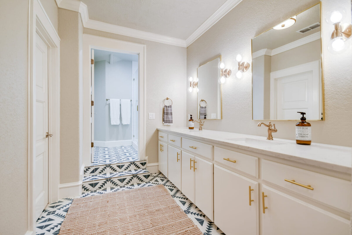 White bathroom with decorative tile and gold mirrors