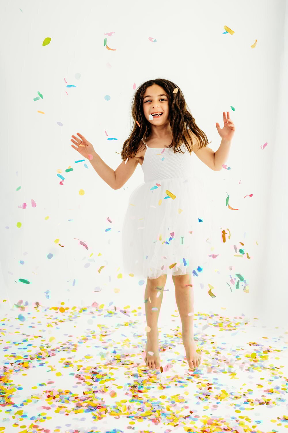 little girl in white dress dances around in confetti