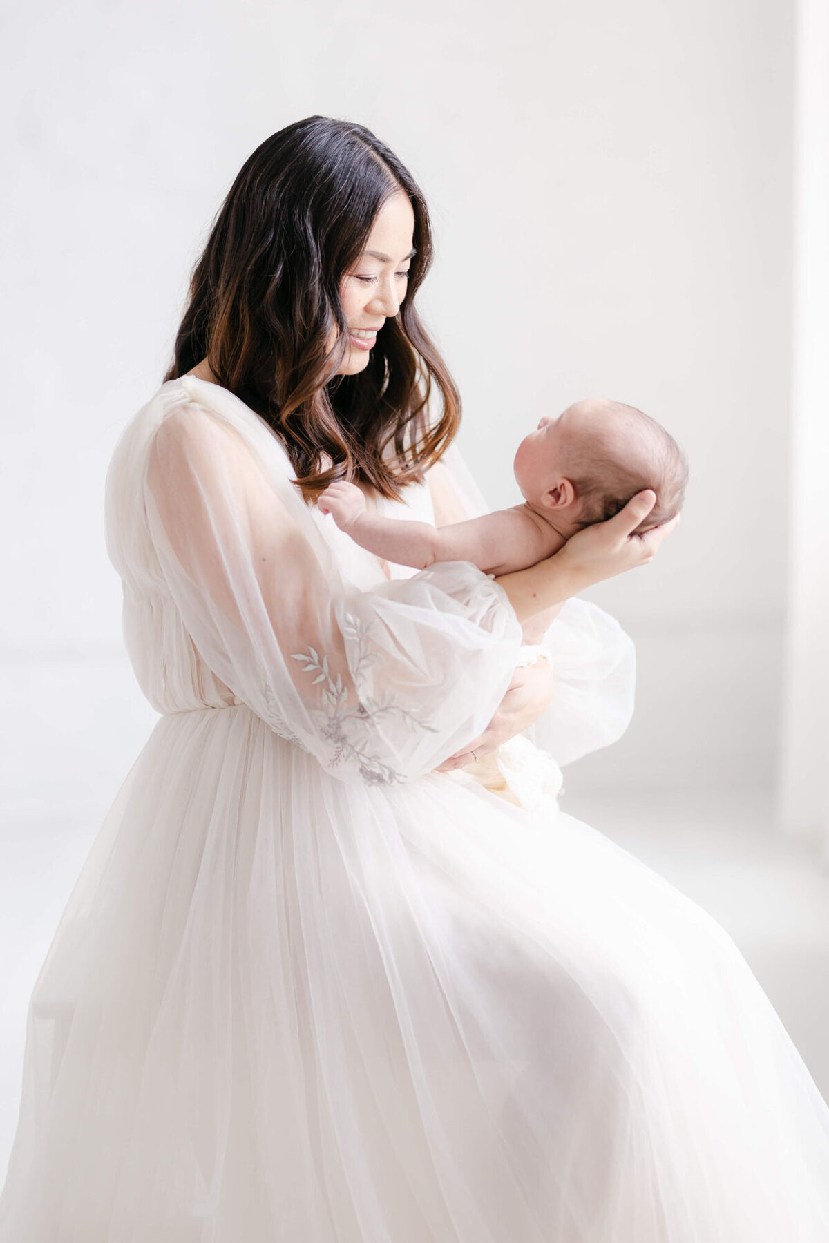 Mother holding newborn against neutral backdrop, Bay Area newborn photographer session.