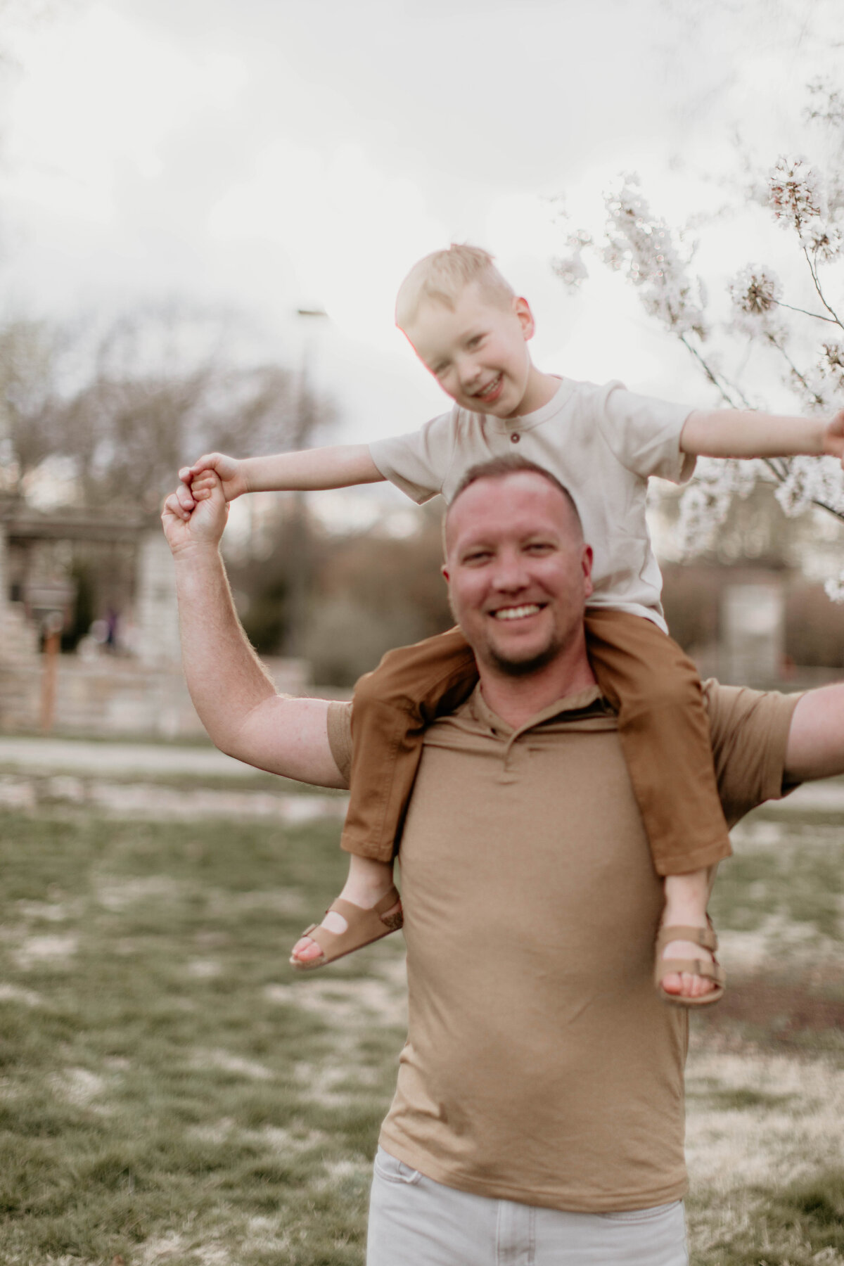 Boy on dad's shoulders under a blooming spring tree.