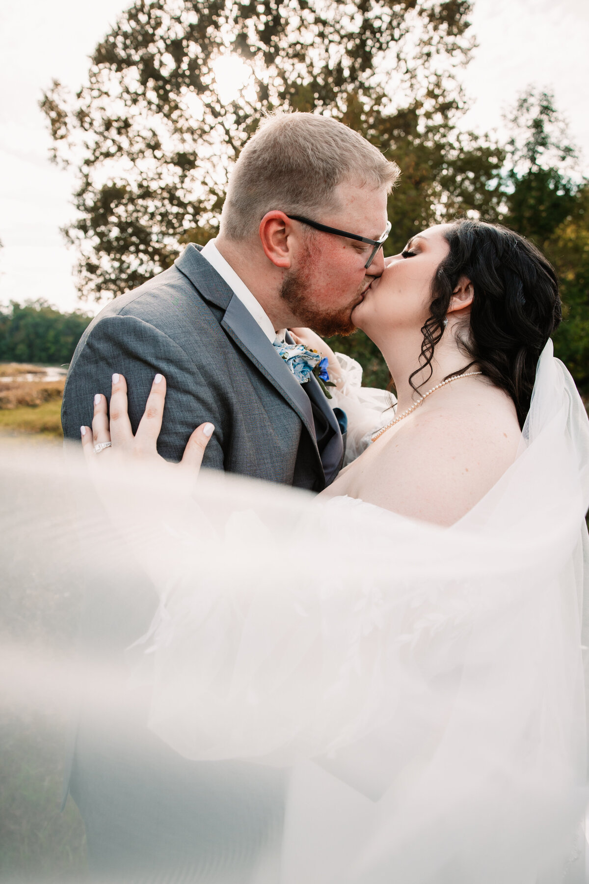 Newlyweds kiss while the veil flies around them at sunset