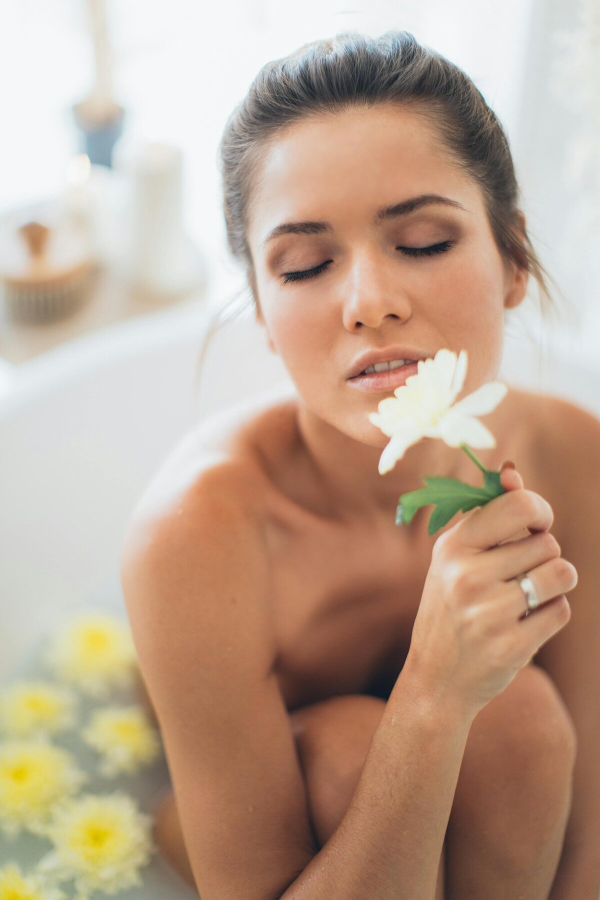 Woman enjoying self care by soaking in the tub and holding a flower