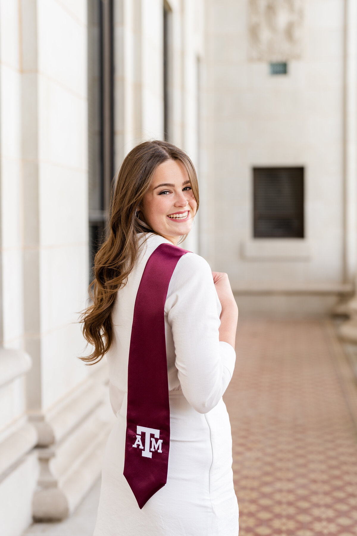 Texas A&M senior girl holding Aggie stole over shoulder and smiling within the columns of the Administration Building