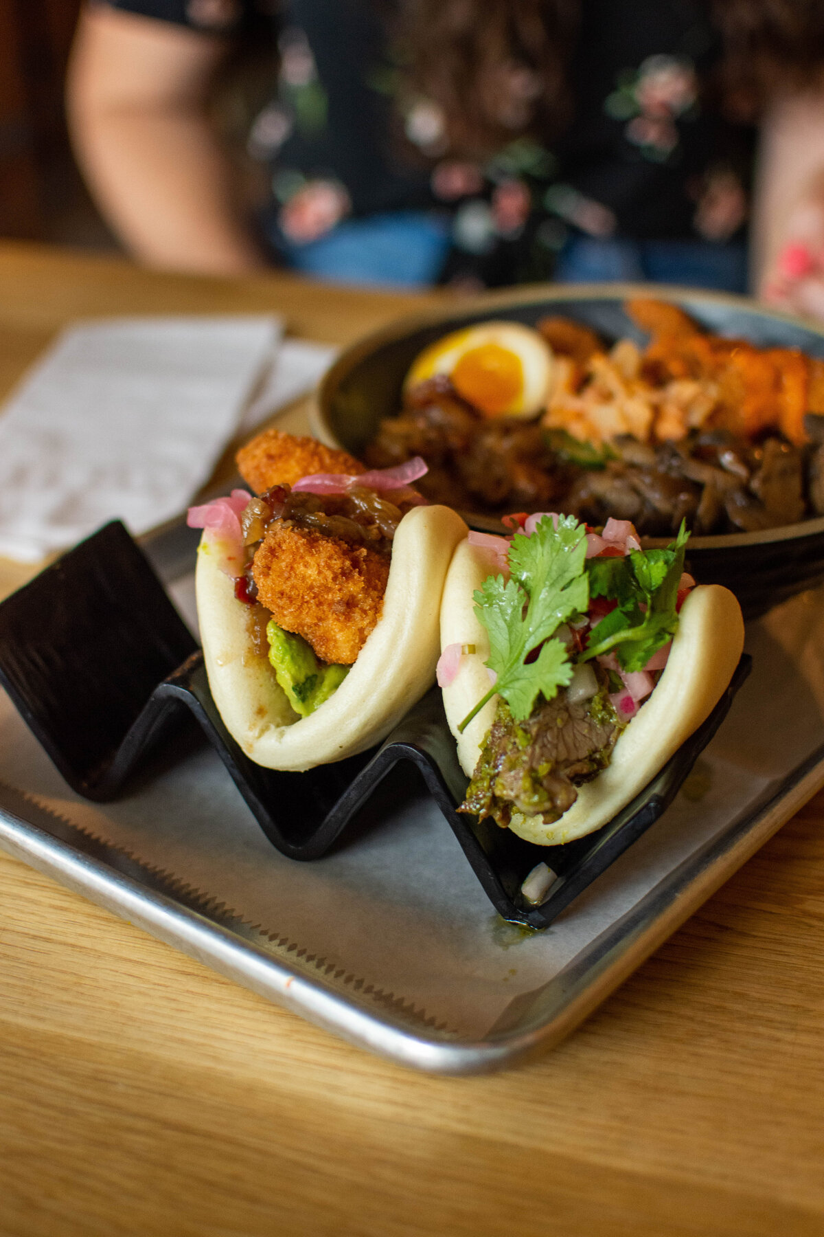 Two baos in a black bao bun holder with rice bowl in the background