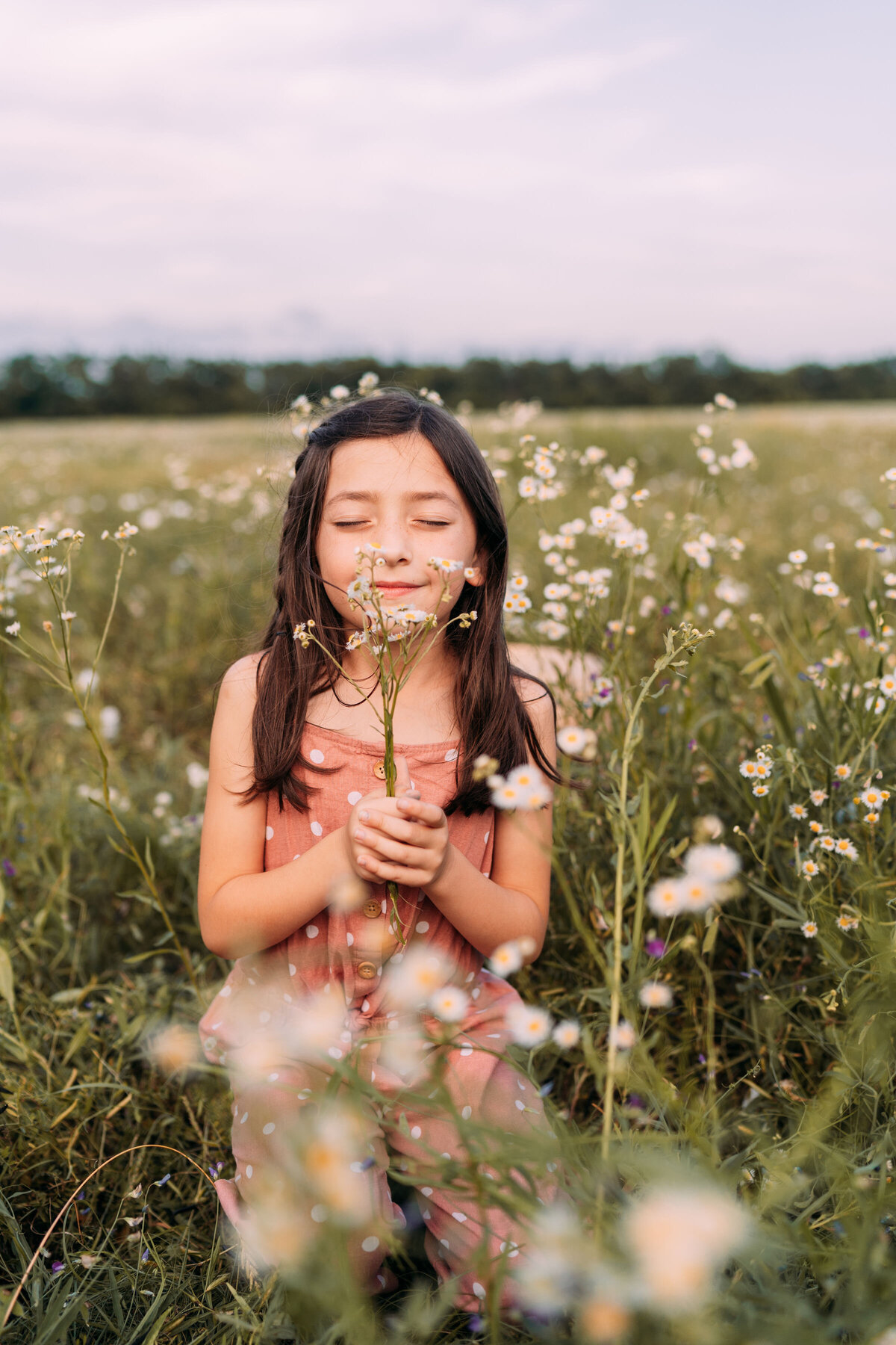 girl smells wildflowers while holding them in her hands with eyes closed