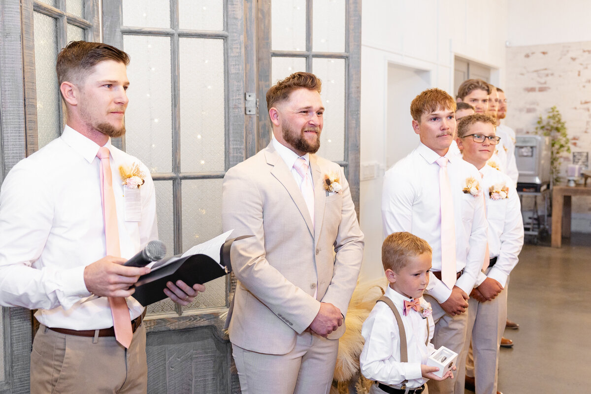 The groom, standing at the altar, sees his bride for the first time as she walks down the aisle. His emotional expression is captured alongside his groomsmen and the officiant, as they eagerly await the ceremony to begin.
