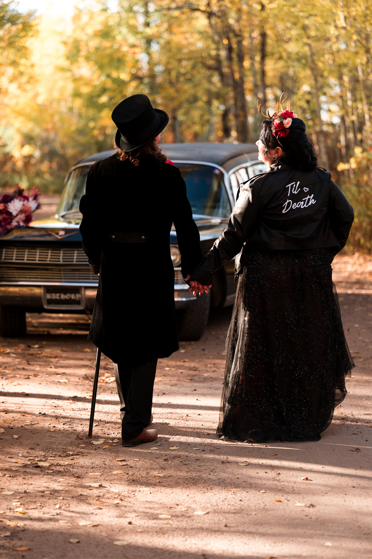 bride and groom walking away, bride is wearing a leather jacket that says til death, groom is wearing a top hat, perfect for an alternative wedding