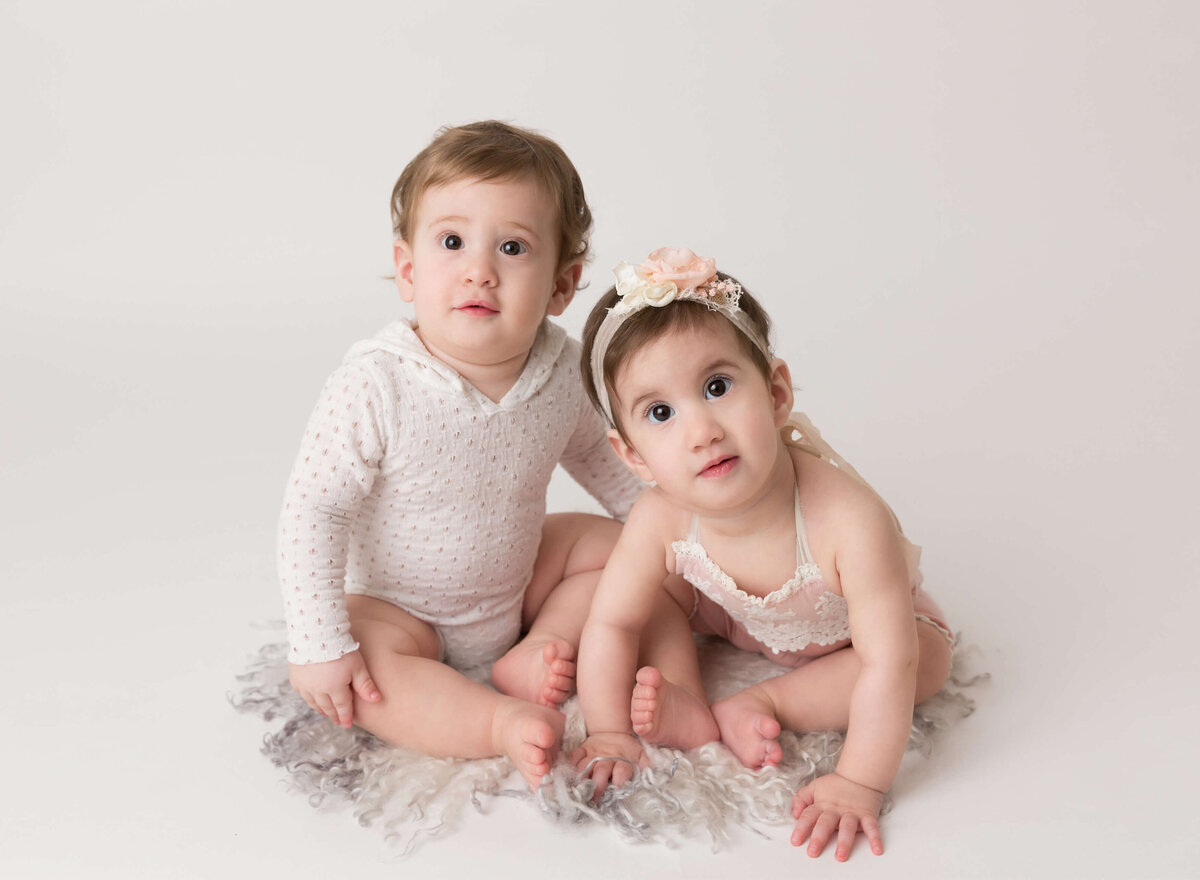 6-month-old twin babies smiling at the camera during their milestone photoshoot in New York City. Professional NYC baby photographer documenting precious memories