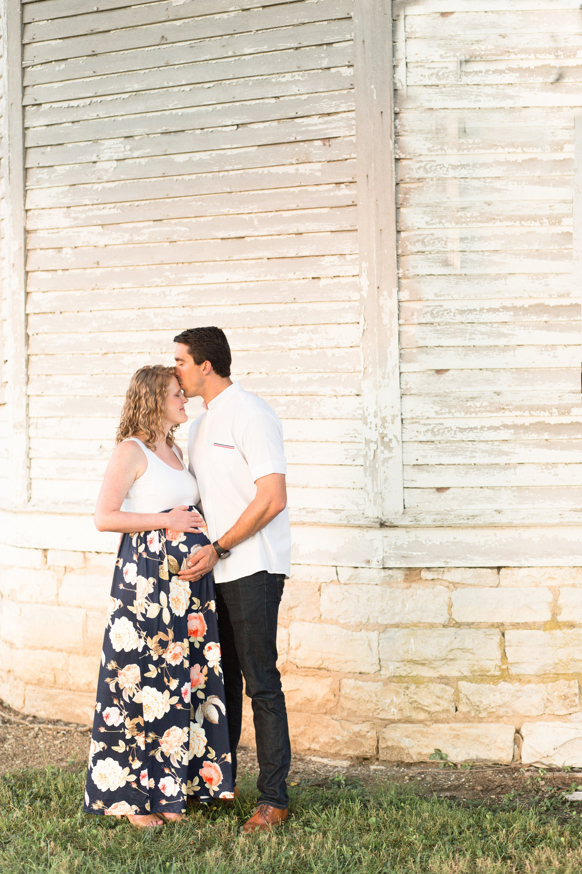 expectant couple embraces by white barn