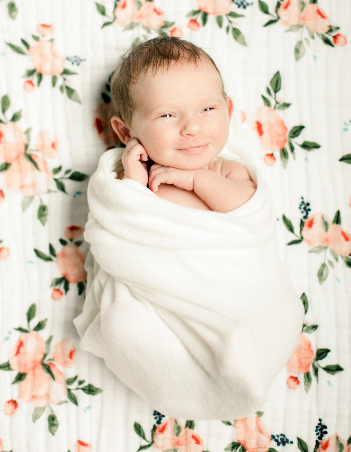 smiling newborn baby girl swaddled on floral blanket