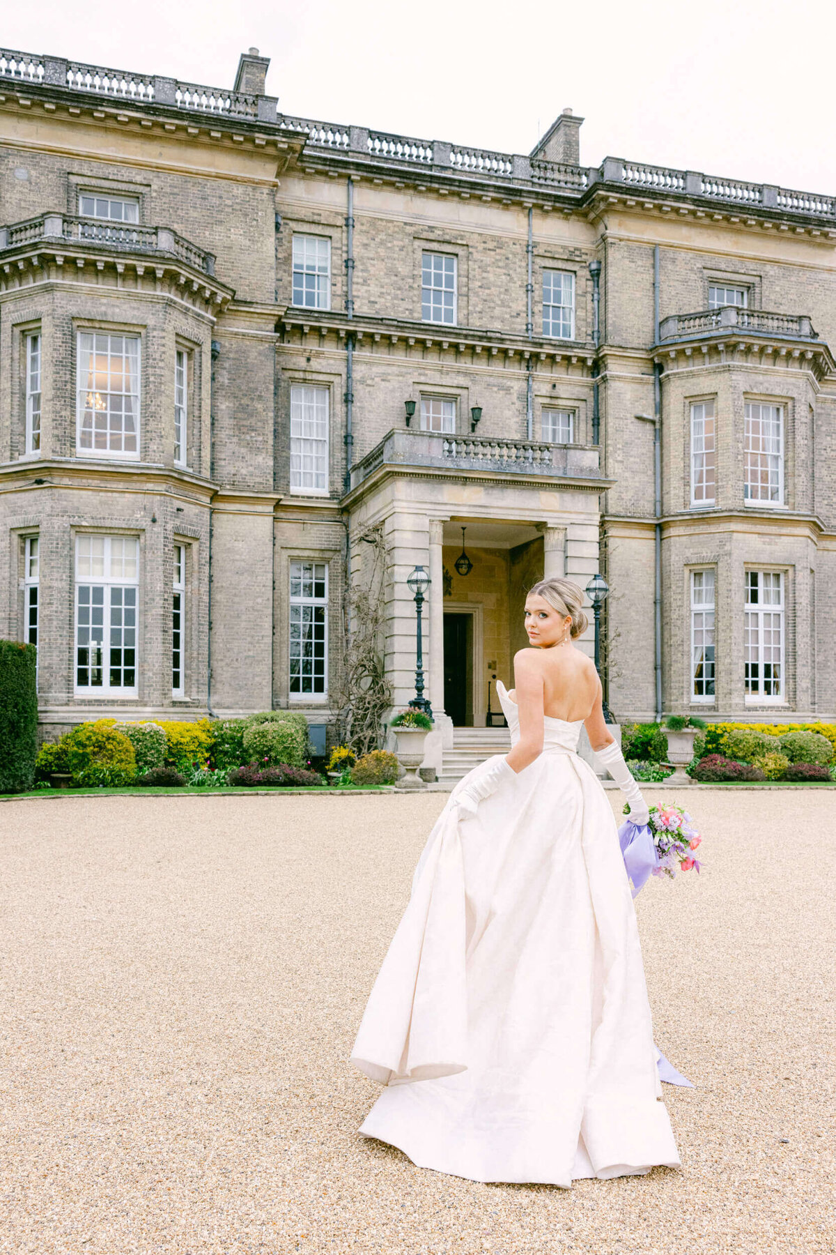 A wedding day photo of the bride in her white dress with Hedsor House behind her