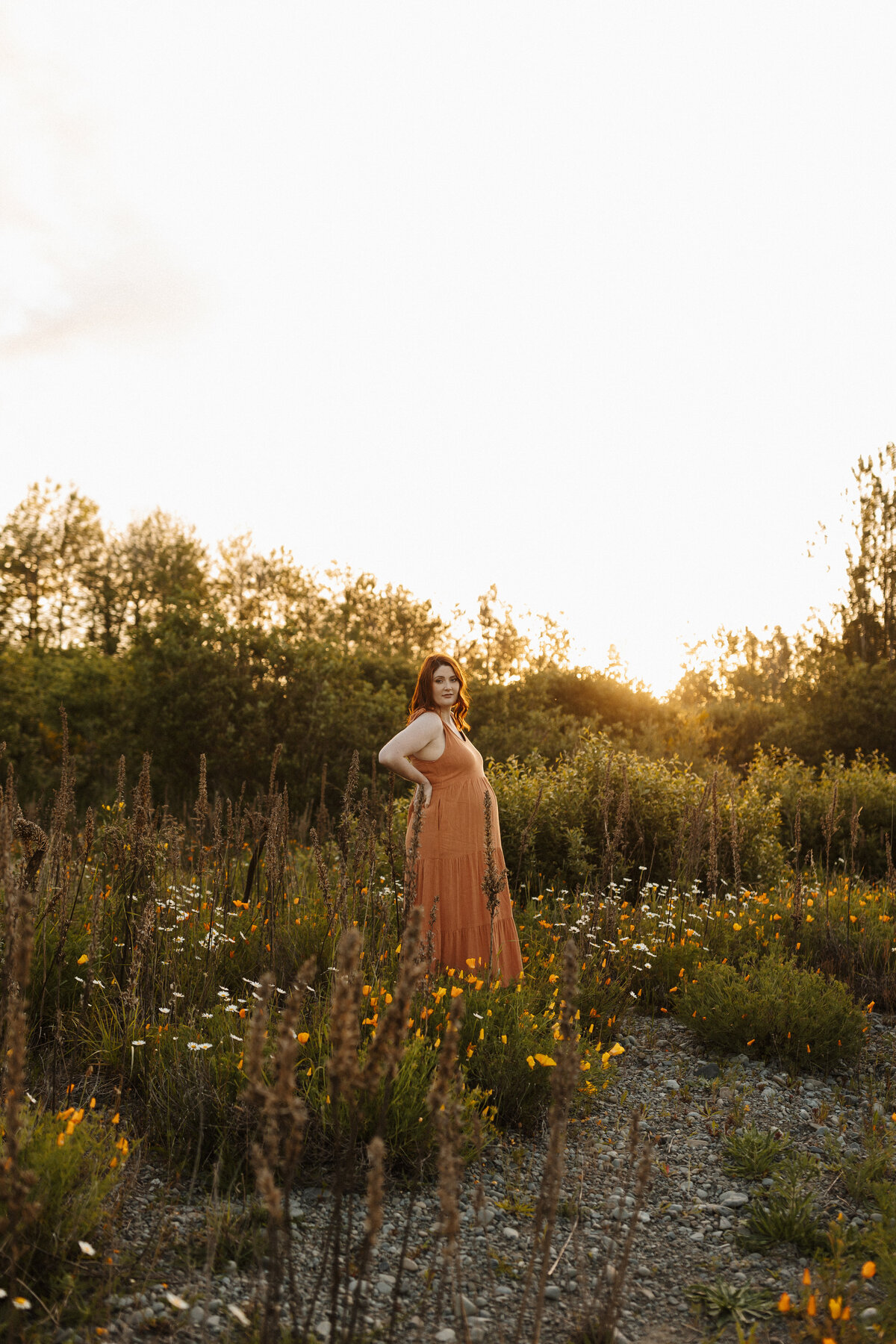a red headed woman stands in a field of flowers during a christchurch maternity photoshoot with lucy jane photography