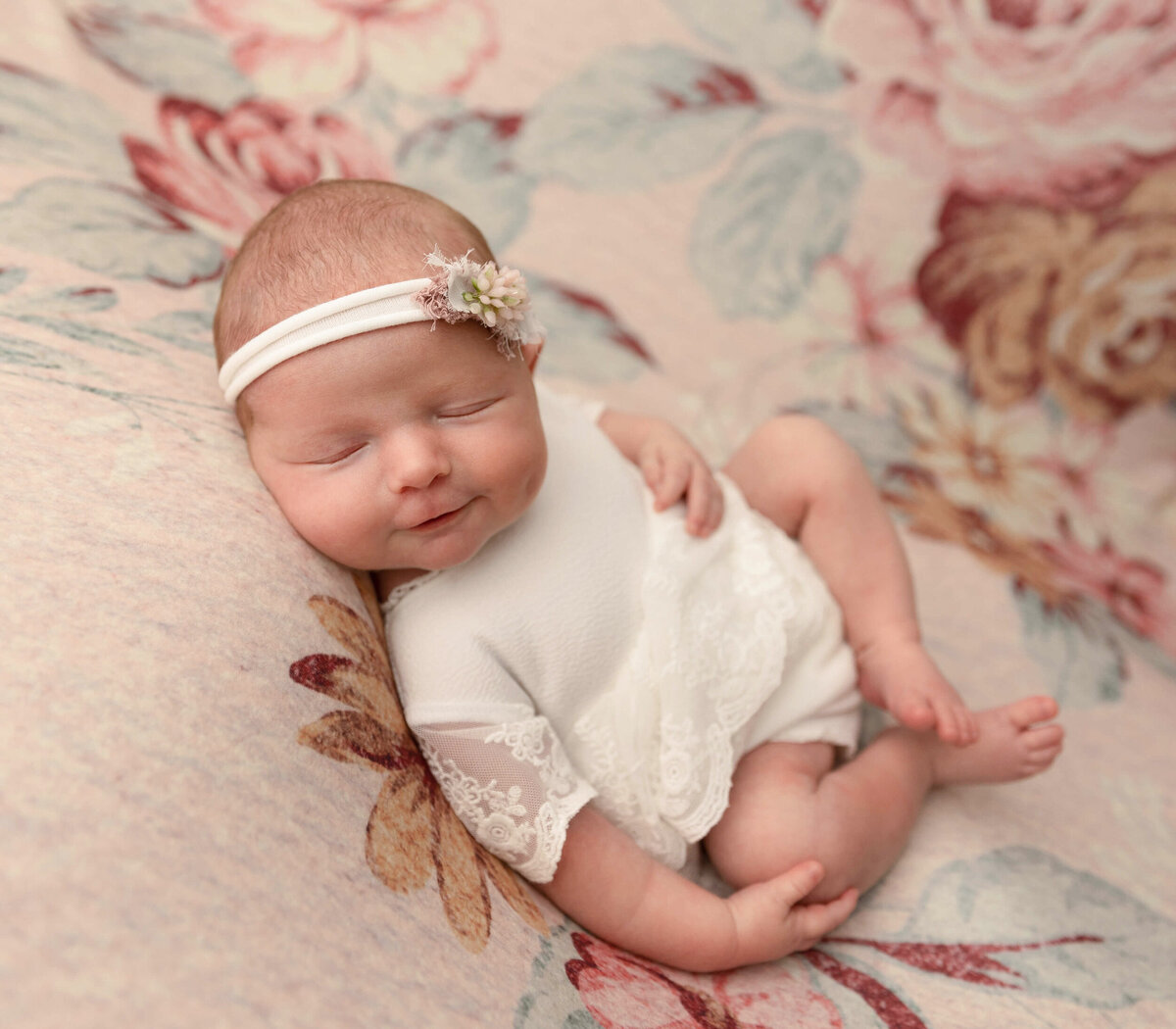 Newborn baby girl in a white dress on a flower backdrop in an Erie PA photography studio